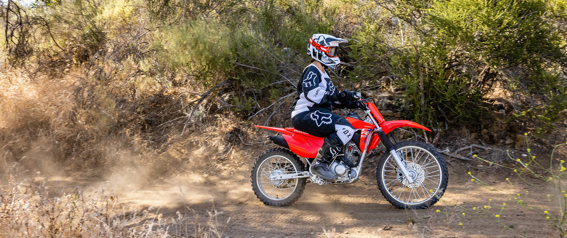 Honda CRF125F dirt bike with black and red bodywork, knobby tires, and handlebar controls, shown from a side angle.