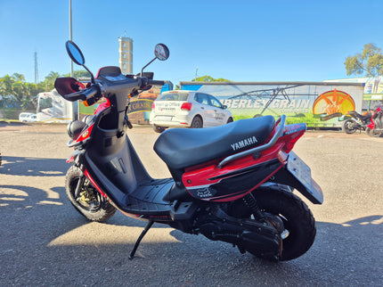 Used 2005 Yamaha BWS 100 scooter, black with silver accents, parked on street, showing side view and handlebar details.