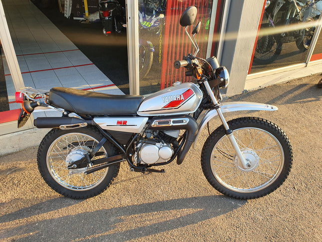 Used Yamaha 1980 MR 50 motorcycle, side view showing black and silver body with seat and handlebars.